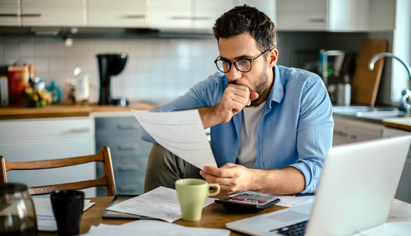 A man reviews financial statements in his kitchen.